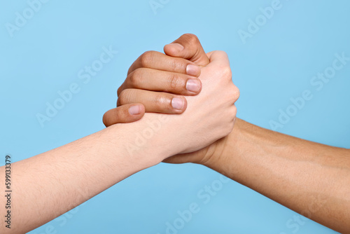 International relationships. People clasping hands on light blue background, closeup