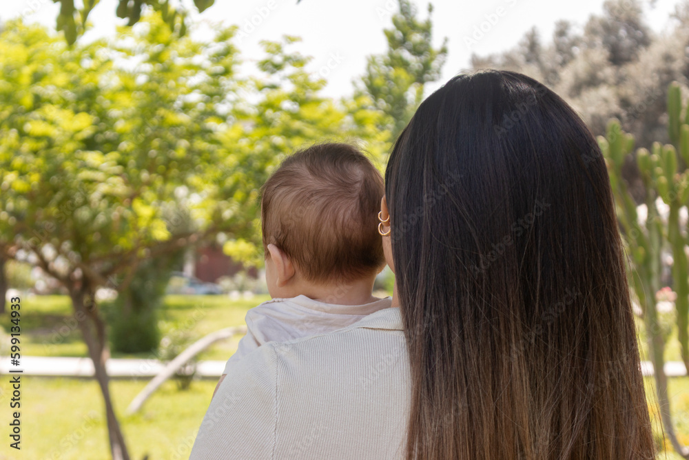 Madre y bebé en el parque, de espaldas, cabello lacio, día de verano Madre y bebé en el parque, de espaldas, cabello lacio, día de verano
