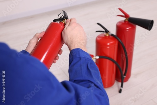 Man checking quality of fire extinguishers indoors, closeup
