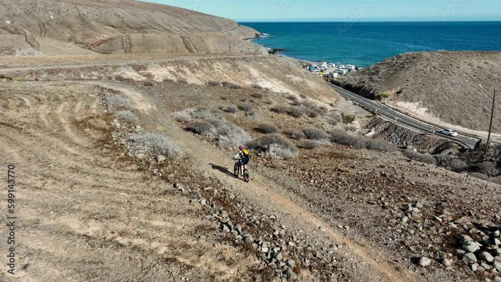 fantastic lateral aerial shot of a man with his mountain bike in a desert landscape and where you can see the coast and the sea. On the island of Gran Canaria, Arguineguin, on a sunny day. fantastic lateral aerial shot of a man with his mountain bike in a desert landscape and where you can see the coast and the sea. On the island of Gran Canaria, Arguineguin, on a sunny day.