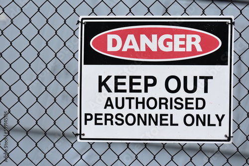 Danger Keep out Authorised personnel only sign black wire fence light grey background copy space 