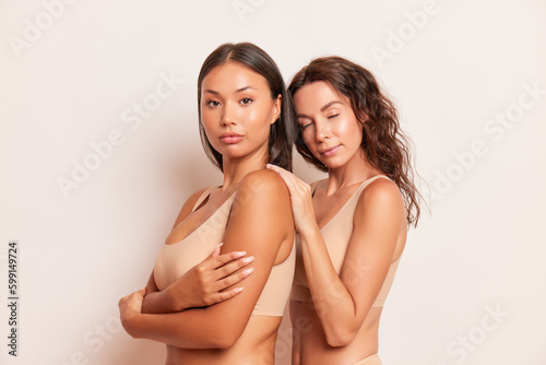 Couple beautiful young woman pose body half-turned on white background, both wearing comfortable underwear, relationship concept, copy space © South House Studio