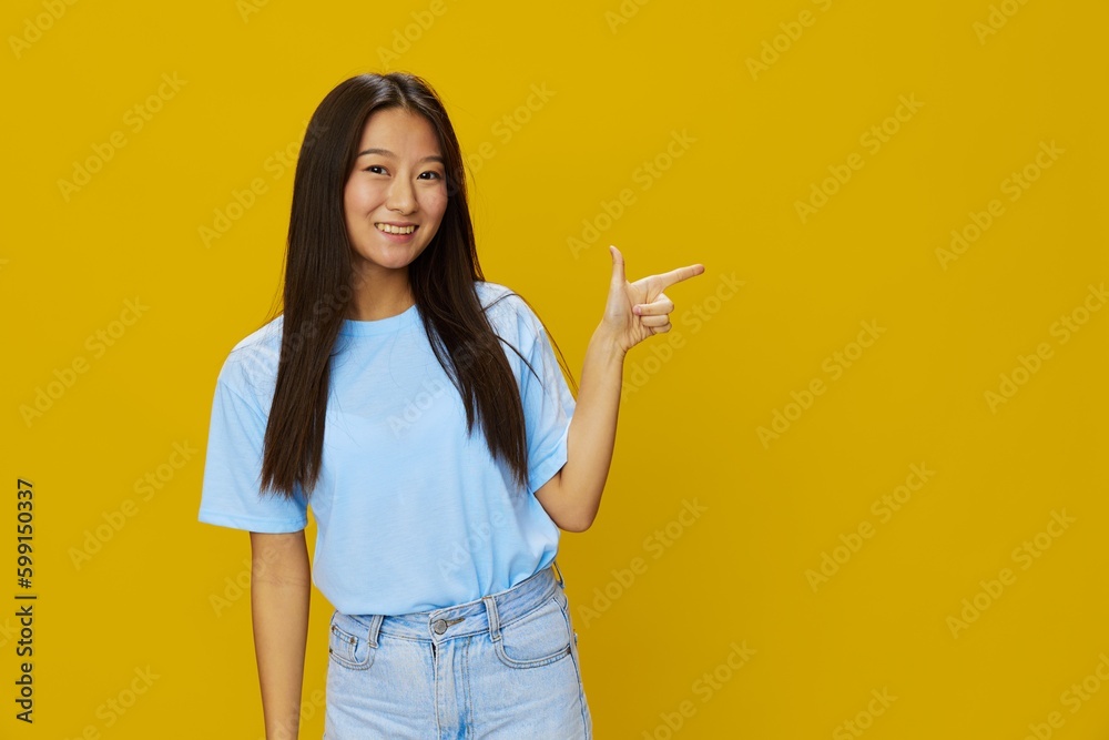 Asian woman smile with teeth hand gestures, signs and symbols on yellow background in blue t-shirt and jeans Asian woman smile with teeth hand gestures, signs and symbols on yellow background in blue t-shirt and jeans