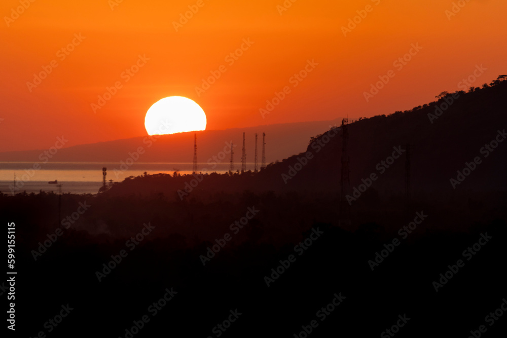 Obraz premium Sun rising behind mountain above the ocean in Indonesia