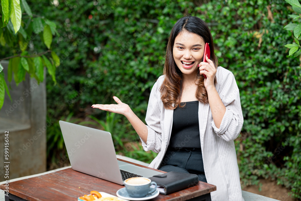 Asian businesswoman using a mobile phone with laptop, notebook, and cup of coffee on the table Asian businesswoman using a mobile phone with laptop, notebook, and cup of coffee on the table