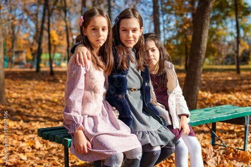 portrait of girls in an autumn city park, children sitting on a bench, talking and enjoying the beautiful nature, talking and playing together, picking yellow leaves
