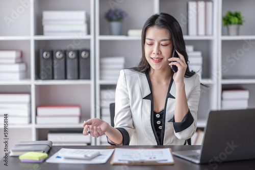 Cheerful business Asian woman freelancer making telephone call share good news about project working in office workplace, business finance concept.	