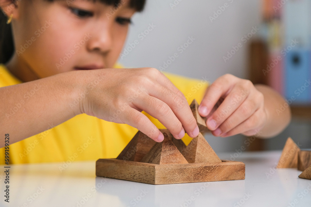 Asian cute little girl playing with wooden toy jigsaw puzzle pyramid on table. Healthy children training memory and thinking. Wooden puzzles are games that increase intelligence for children. 