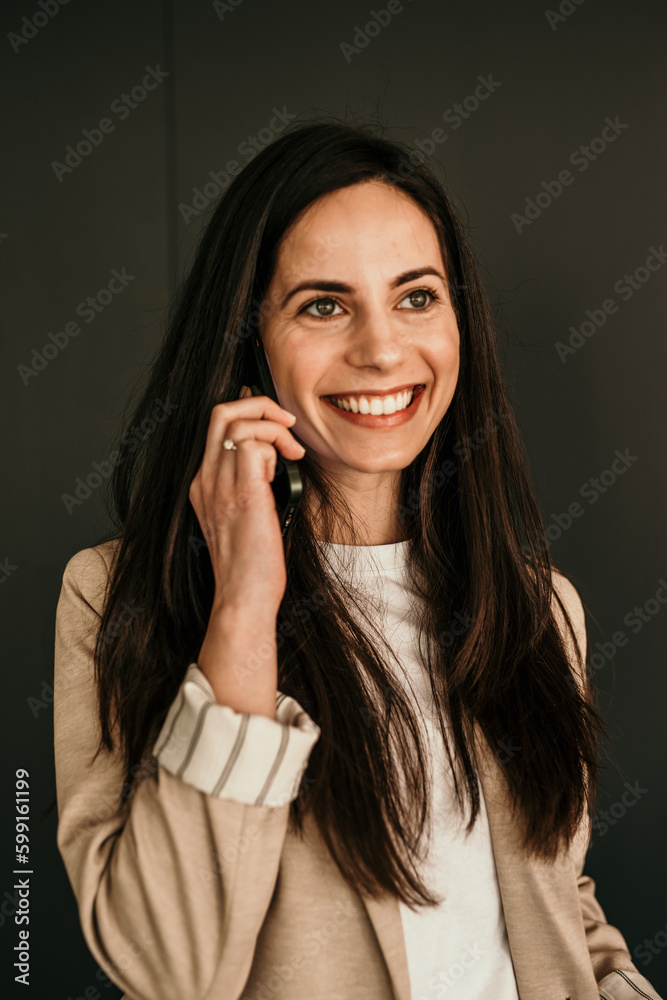Cheerful woman in a business outfit talking on the phone with a big smile against the studio background. Cheerful woman in a business outfit talking on the phone with a big smile against the studio background.