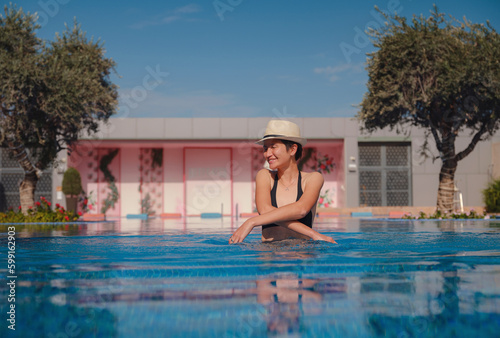 Portrait of beautiful asian woman in black swimwear and hat relaxing in swimming pool spa. Hot summer day and bright sunny light. Healthy body care in travel © YURII Seleznov