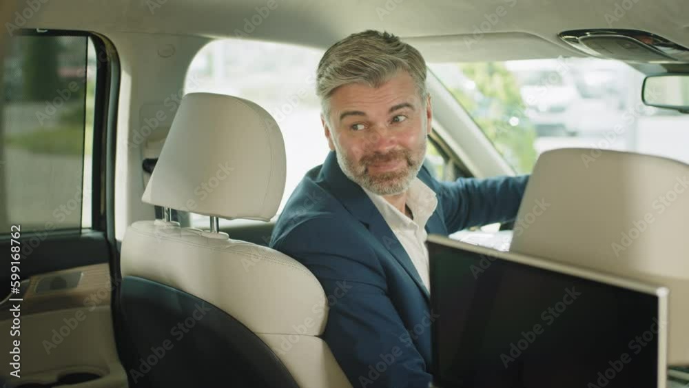 Driving man inside a modern new car. Rear view. Reflection of businessman in mirror in a car showroom. Happy 45s man wearing formal wear in new car turning around, smiling looking at camera. Driving man inside a modern new car. Rear view. Reflection of businessman in mirror in a car showroom. Happy 45s man wearing formal wear in new car turning around, smiling looking at camera.