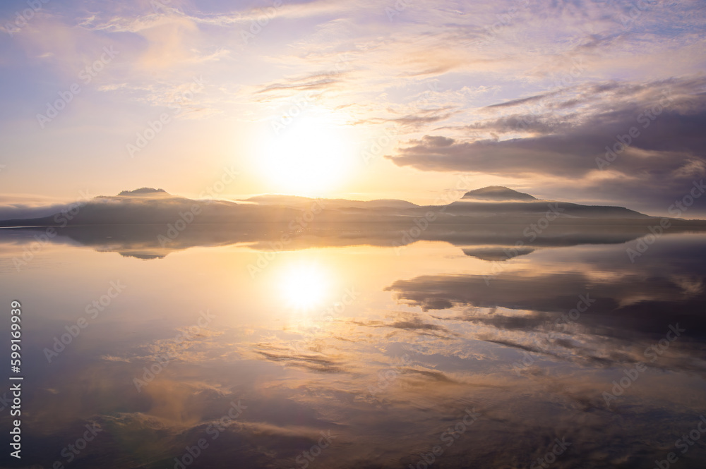 朝日の輝く空を水面に反射する湖。北海道の屈斜路湖。