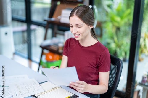 Young successful employee business woman in red shirt hold paper account documents work stand at workplace white desk with laptop pc computer at light modern office indoors achievement career concept © ND STOCK