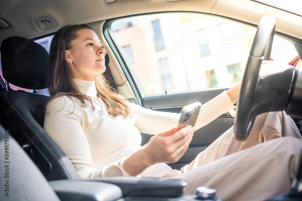 Young woman sitting in car and using smart phone, business woman busy driving