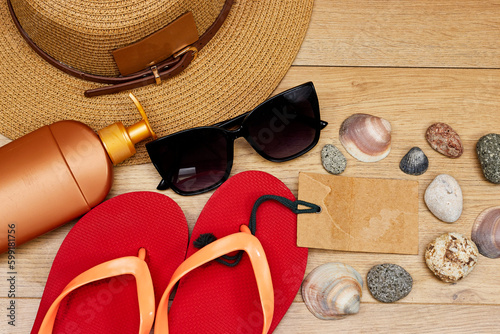 orange beach slippers and hat, sunglasses, bottle of cream sun with seashells and stones, empty tag  on wooden table photo