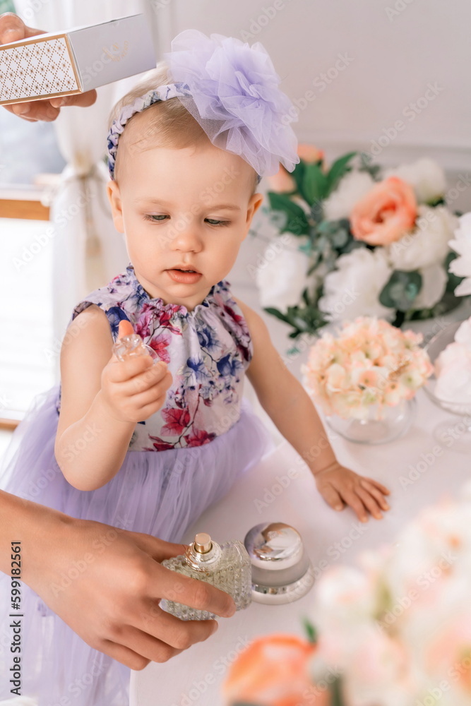Baby girl elegant dress. A one year old girl in a puffy dress and a cute bow poses against the backdrop of a bright room with a dressing table and flowers. Stock Photo