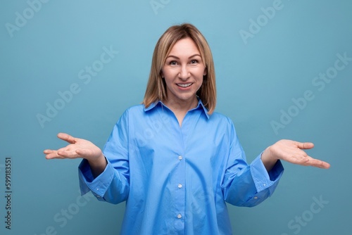 portrait of a confident neat european blond woman in a shirt with open arms on a blue background with copyspace