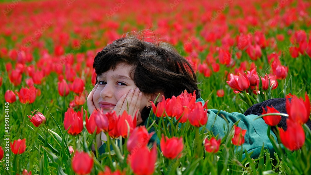 Naklejka premium Boy stretching in a field of tulips.