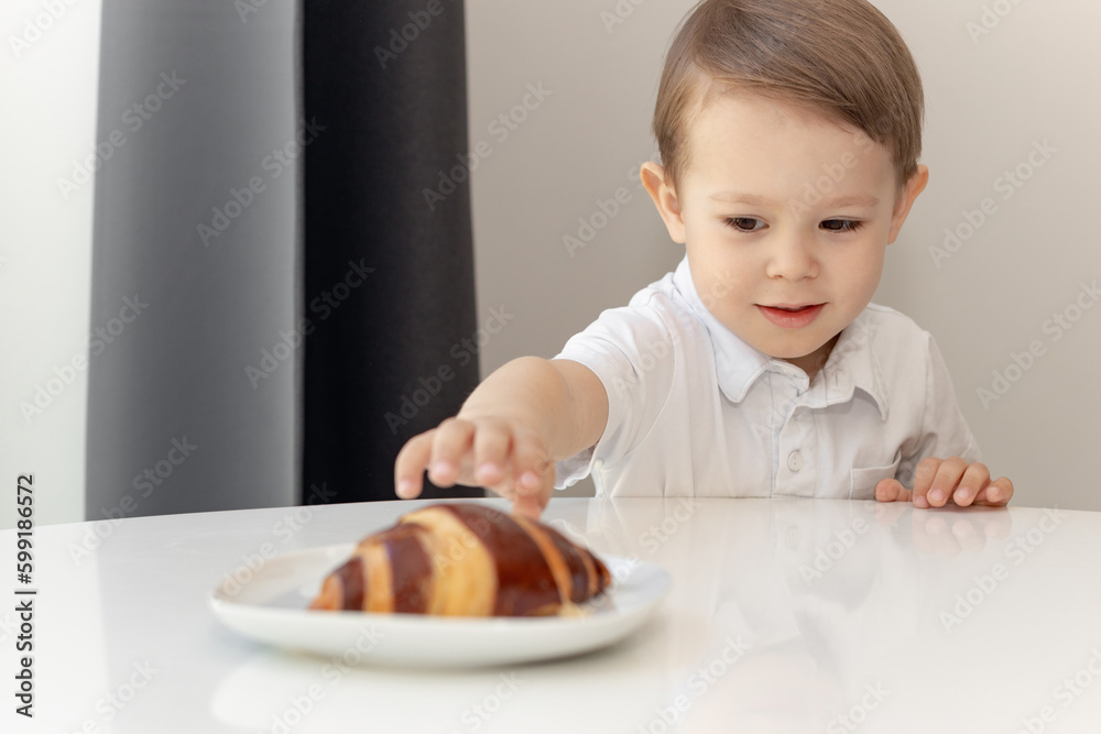 The concept of children and sweets. Cute little boy wants to eat a chocolate croissant, the child is craving a bun The concept of children and sweets. Cute little boy wants to eat a chocolate croissant, the child is craving a bun