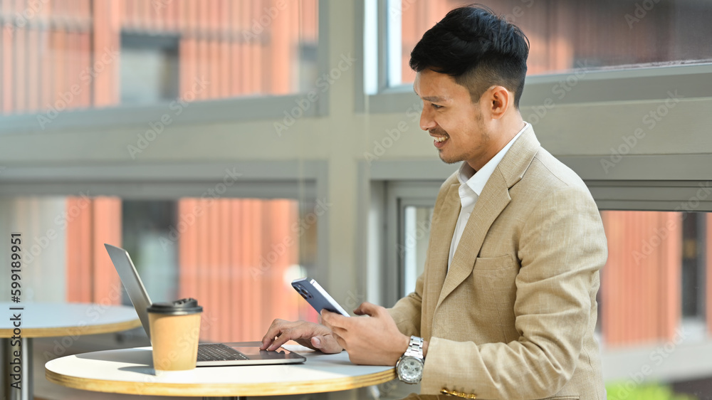 Successful businessman holding smartphone and working online on laptop computer