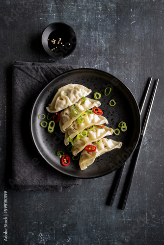 A plate with fresh gyoza dumpling on black plate and background with chopsticks