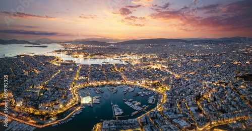 Aerial panorama of the illuminated Piraeus district in Athens, Greece, with Zea Marina and the ferry boat harbour in the background during evening time