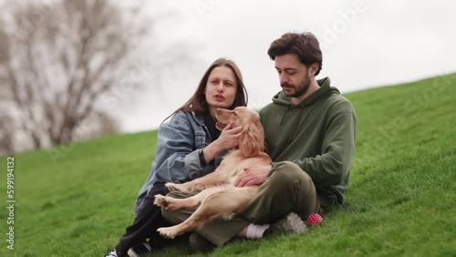 Young couple talking and playing with dog. Dog owners sitting on the grass with their pet