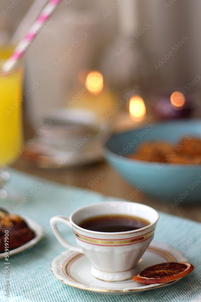 Plate of chocolate pralines, bowl of cookies, cups of tea, glasses of juice and lit candles on the table. Selective focus. Plate of chocolate pralines, bowl of cookies, cups of tea, glasses of juice and lit candles on the table. Selective focus.