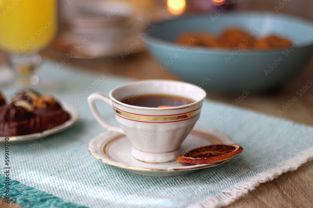 Fototapeta premium Plate of chocolate pralines, bowl of cookies, cups of tea, glasses of juice and lit candles on the table. Selective focus.
