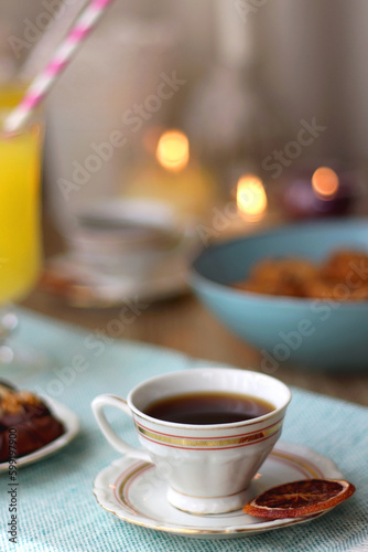 Plate of chocolate pralines  bowl of cookies  cups of tea  glasses of juice and lit candles on the table. Selective focus.