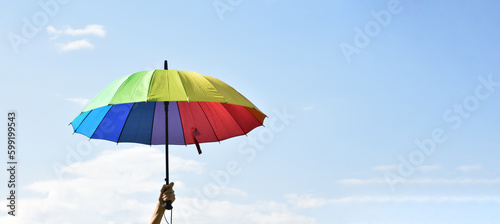 Fototapeta Naklejka Na Ścianę i Meble -  Rainbow umbrella holdingin hand against bluesky, copy space, concept for LGBT celebrations in pride month, June, around the world.
