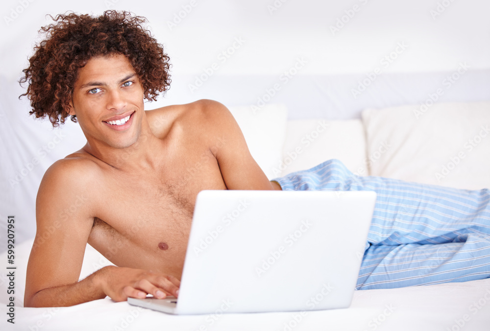 Getting the day started online. Portrait of a handsome young ethnic man lying on a bed and using his laptop.
