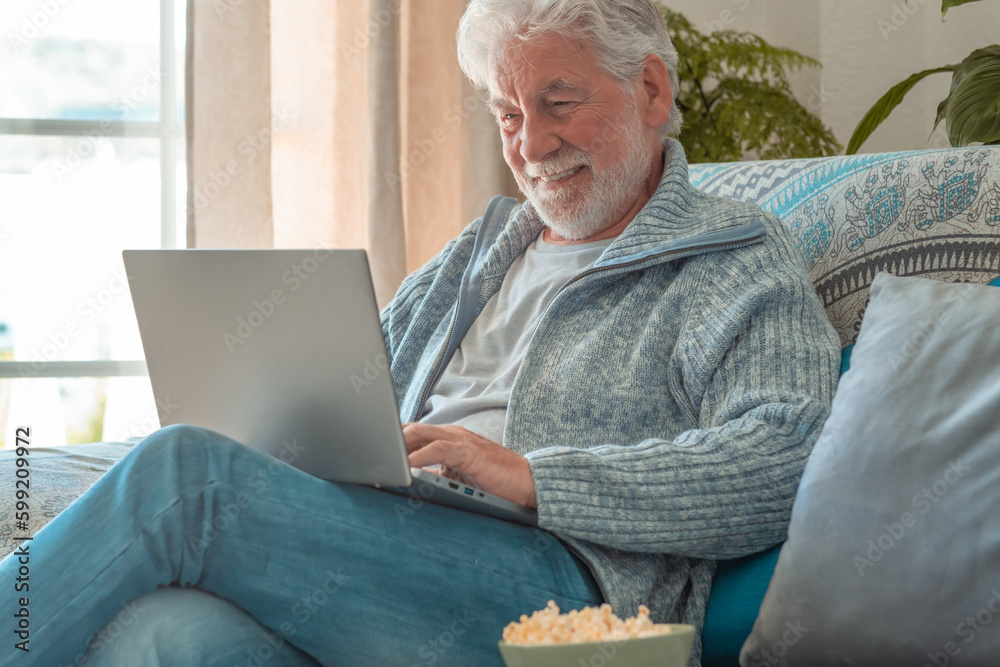 Happy elderly 70s man seated on sofa video chatting by laptop, older generation and modern tech application easy usage concept Happy elderly 70s man seated on sofa video chatting by laptop, older generation and modern tech application easy usage concept