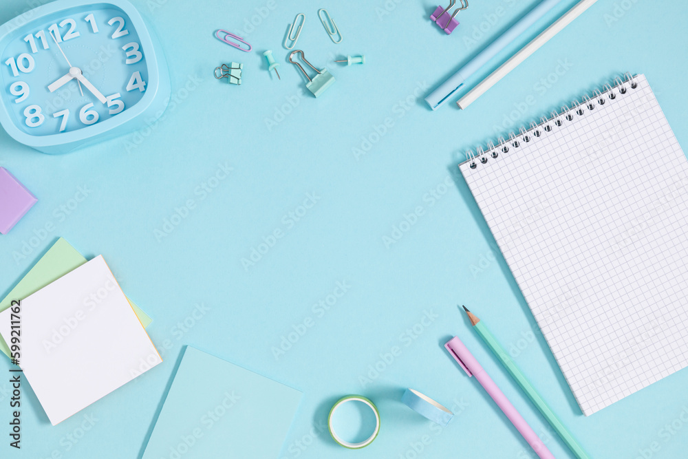 Back to school concept. Flat lay top view of stationery notepad alarm clock pens pencils paper clips sticky tape note paper isolated on pastel blue background Back to school concept. Flat lay top view of stationery notepad alarm clock pens pencils paper clips sticky tape note paper isolated on pastel blue background