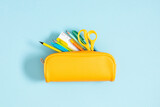 Back to school concept. Flat lay top view on yellow full pencil case with pencils and pens notepad scissors isolated on pastel blue background