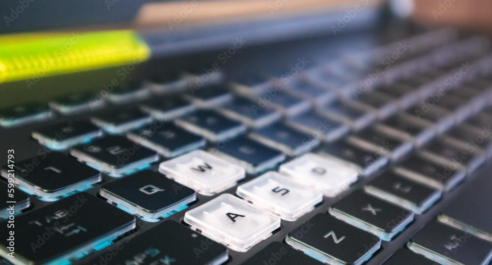 Highlighted gaming keys with blue light and focus blur. Powerful dark notebook keyboard close-up. Tech, IT, e-sport, computer science background Highlighted gaming keys with blue light and focus blur. Powerful dark notebook keyboard close-up. Tech, IT, e-sport, computer science background