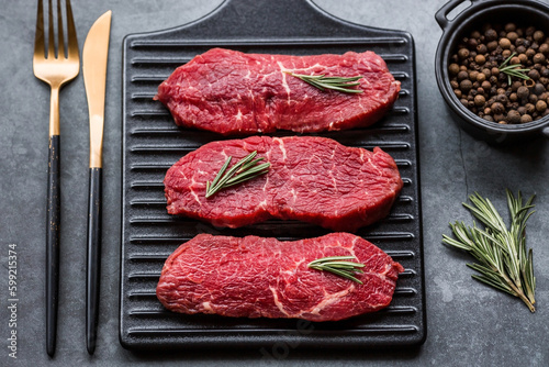 Fresh meat. Raw beef steaks with rosemary and spices on a stylish blackboard. Flat top view.