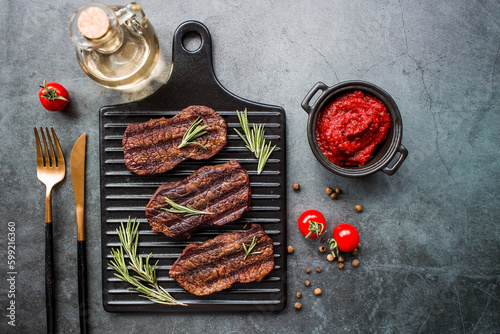 Fresh meat. Grilled beef steaks with rosemary, spices and tomato paste on a stylish board. Flat top view.