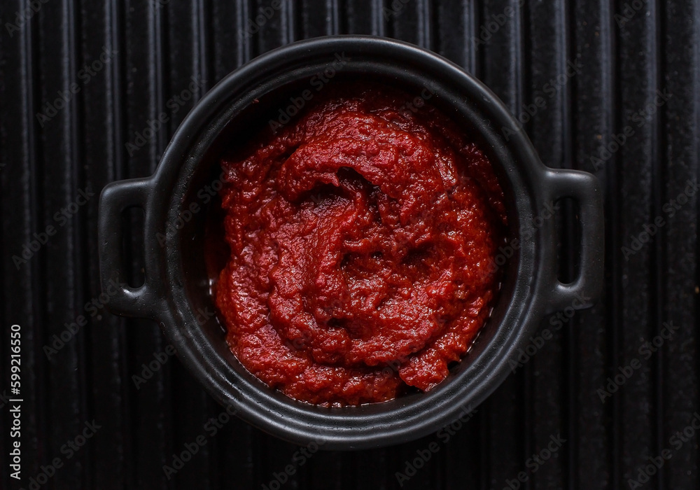 Tomato paste in a stylish black sauce pan on a ceramic dish. Preparation of seasoning, sauce. Canning vegetables. Tomato paste in a stylish black sauce pan on a ceramic dish. Preparation of seasoning, sauce. Canning vegetables.