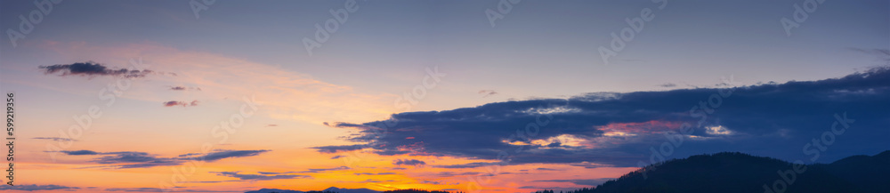 sky panorama at dusk. glowing clouds above the mountain silhouette in evening light