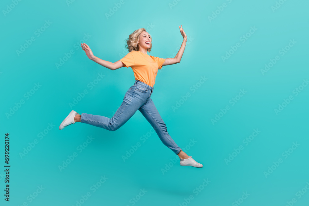 Full length photo of excited funky girl wear orange t-shirt jumping high empty space isolated turquoise color background