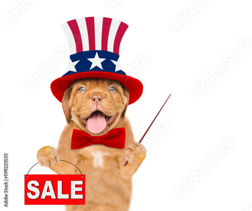 Happy Mastiff puppy wearing like Uncle Sam points away on empty space and shows signboard with labeled "sale". isolated on white background © Ermolaev Alexandr