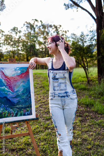 Happy young lady artist with paintbrush tucking hair behind ear photo