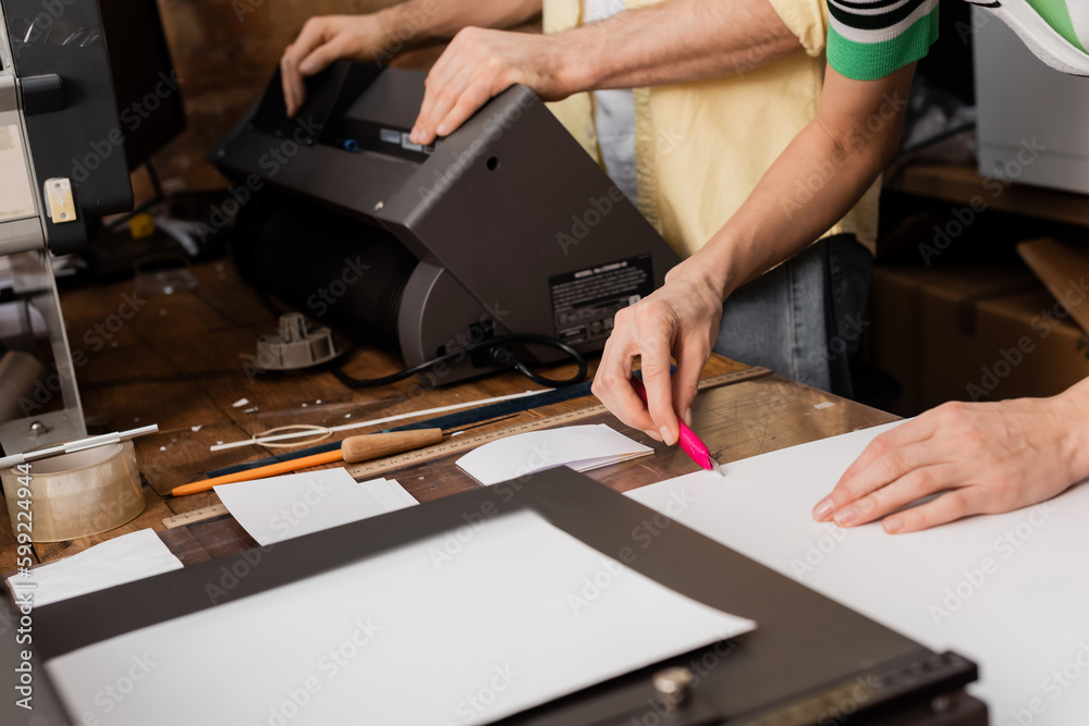 cropped view of typographer cutting paper with knife near colleague in print center. cropped view of typographer cutting paper with knife near colleague in print center.