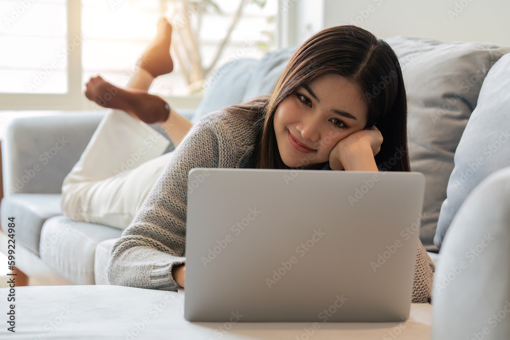 Smiling woman watching video using laptop, relaxing on a couch at home in the living room Smiling woman watching video using laptop, relaxing on a couch at home in the living room