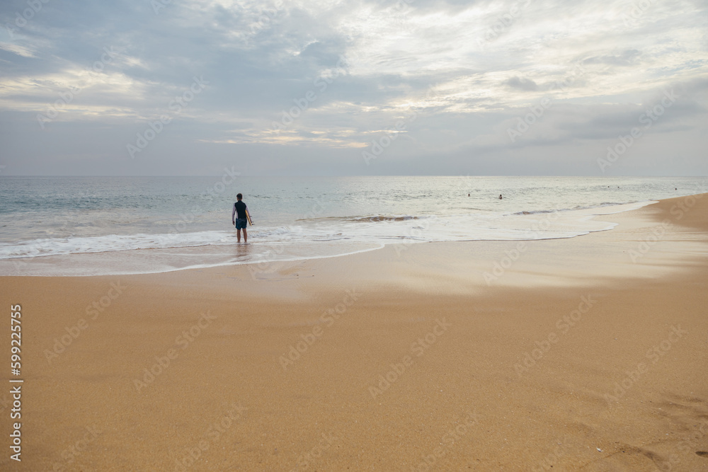 Young boy with a surfboard standing on the sandy ocean beach in the sunset time. Young boy with a surfboard standing on the sandy ocean beach in the sunset time.