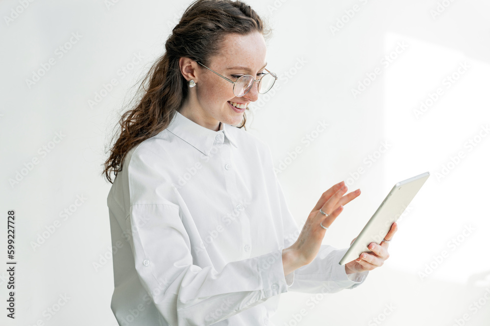 A student uses a tablet for education training, clicks on the screen, smiling cheerful woman in the office stands in modern stylish clothes. A student uses a tablet for education training, clicks on the screen, smiling cheerful woman in the office stands in modern stylish clothes.