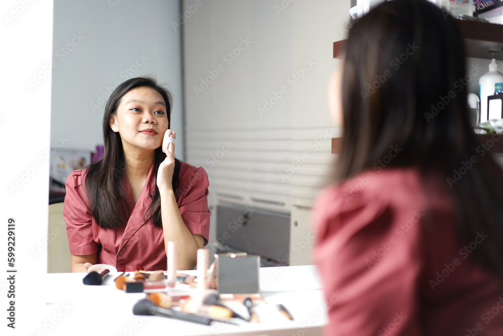 Beautiful Asian woman doing makeup in front of a dressing table mirror Beautiful Asian woman doing makeup in front of a dressing table mirror