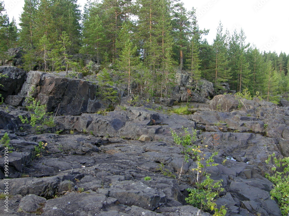 A rocky landscape with trees and rocks in the foreground. Waterfall Poor Porog, Girvas, Republic of Karelia, Russia.