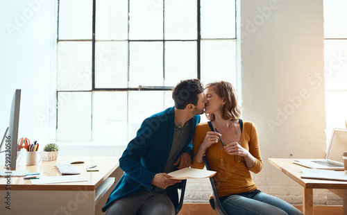 More than an office romance. young couple kissing while working together in their modern office. photo